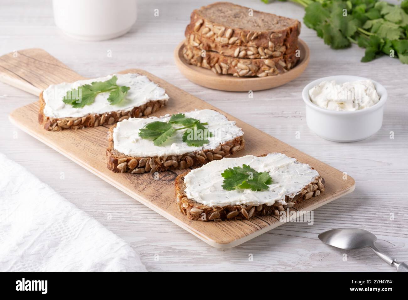 Tranches de pain de grains entiers fraîchement préparées, recouvertes de tartinade crémeuse et garnies de coriandre sur une planche à découper en bois Banque D'Images