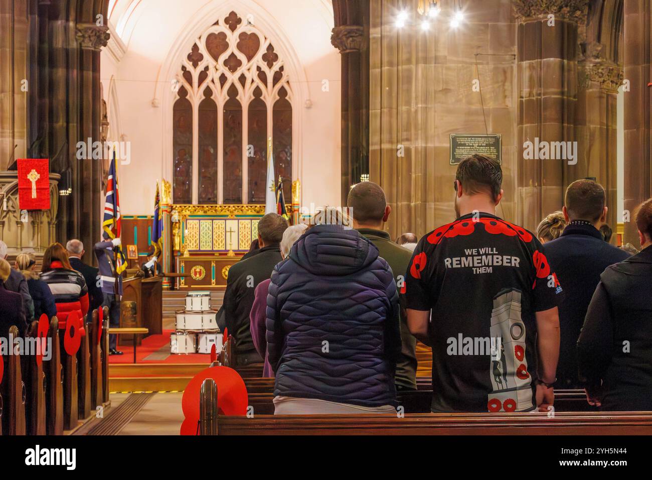 Warrington, Cheshire, Angleterre, Royaume-Uni. 09 novembre 2024. Le festival annuel du souvenir a lieu à l'intérieur de l'église paroissiale St Elphin. Ce fut une soirée pour se souvenir et honorer le service et le sacrifice de nos forces armées dans les conflits mondiaux. Homme portant une chemise avec des coquelicots et 'nous nous souviendrons d'eux' est assis à côté de l'église pour le service. Crédit : John Hopkins/Alamy Live News Banque D'Images