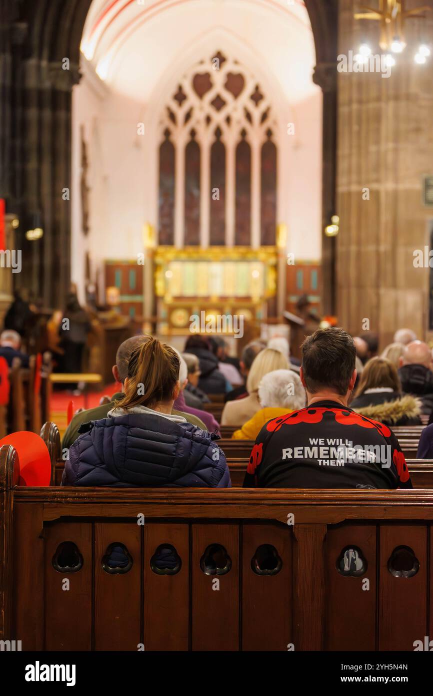 Warrington, Cheshire, Angleterre, Royaume-Uni. 09 novembre 2024. Le festival annuel du souvenir a lieu à l'intérieur de l'église paroissiale St Elphin. Ce fut une soirée pour se souvenir et honorer le service et le sacrifice de nos forces armées dans les conflits mondiaux. Homme portant une chemise avec des coquelicots et 'nous nous souviendrons d'eux' est assis à côté de l'église pour le service. Crédit : John Hopkins/Alamy Live News Banque D'Images