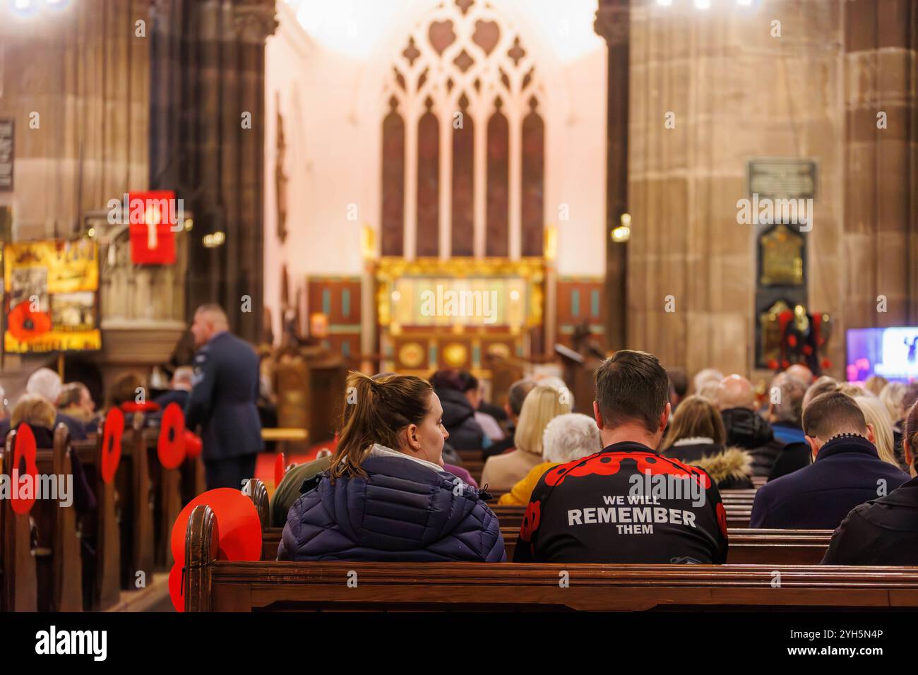 Warrington, Cheshire, Angleterre, Royaume-Uni. 09 novembre 2024. Le festival annuel du souvenir a lieu à l'intérieur de l'église paroissiale St Elphin. Ce fut une soirée pour se souvenir et honorer le service et le sacrifice de nos forces armées dans les conflits mondiaux. Homme portant une chemise avec des coquelicots et 'nous nous souviendrons d'eux' est assis à côté de l'église pour le service. Crédit : John Hopkins/Alamy Live News Banque D'Images