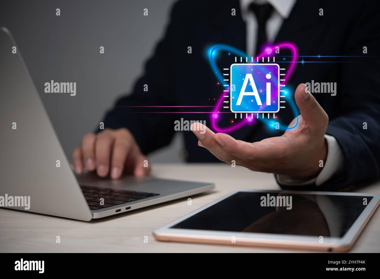 Homme d'affaires présentant une icône lumineuse d'IA au-dessus de sa main, avec un ordinateur portable et une tablette sur le bureau, représentant la technologie de l'intelligence artificielle. Banque D'Images
