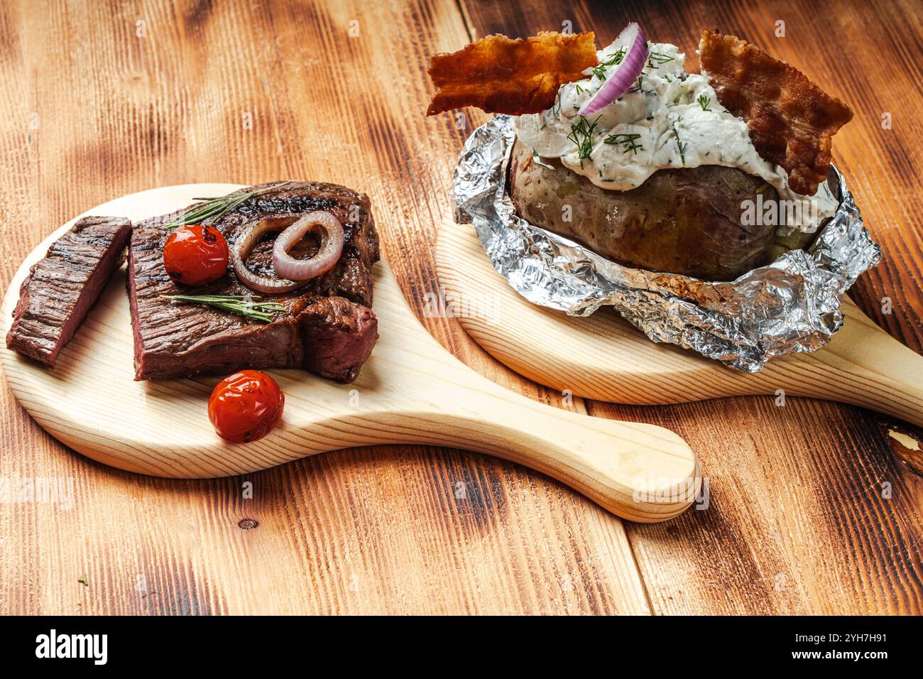 Boeuf rôti avec tomates et pommes de terre cuites dans du papier d'aluminium avec du fromage cottage et des chips de bacon sur un fond en bois. Photo de haute qualité Banque D'Images