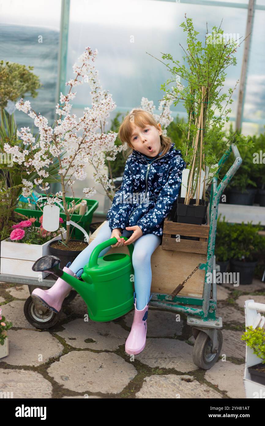 Jeune fille assise dans un panier dans Greenhouse Gardening Center entourée de plantes Banque D'Images