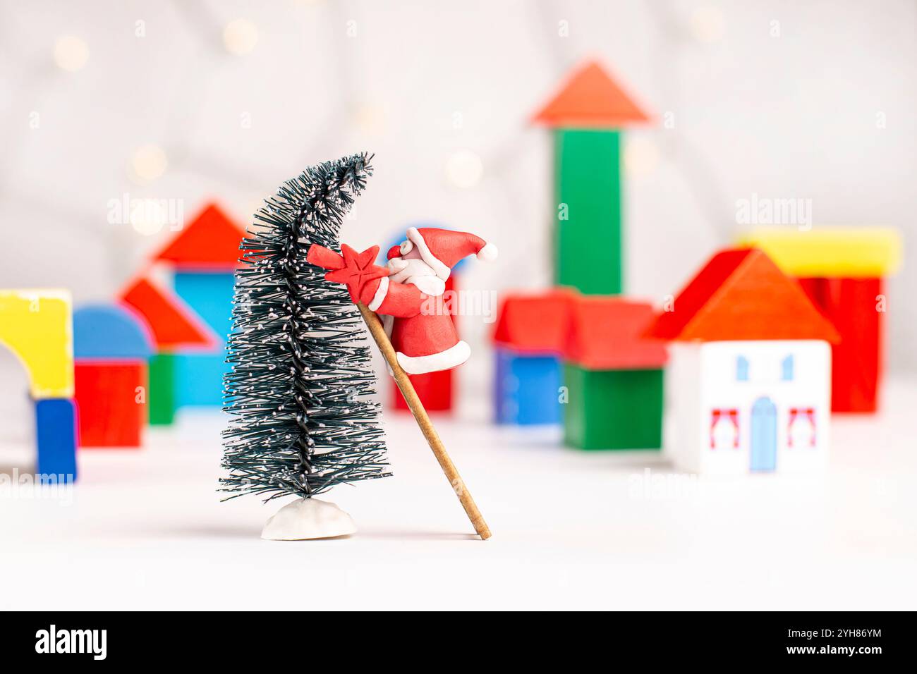 Plasticine Santa Claus essaie d'accrocher une étoile sur un arbre de Noël sur un fond flou d'un village fait de blocs de bois. Noël et New Yea Banque D'Images