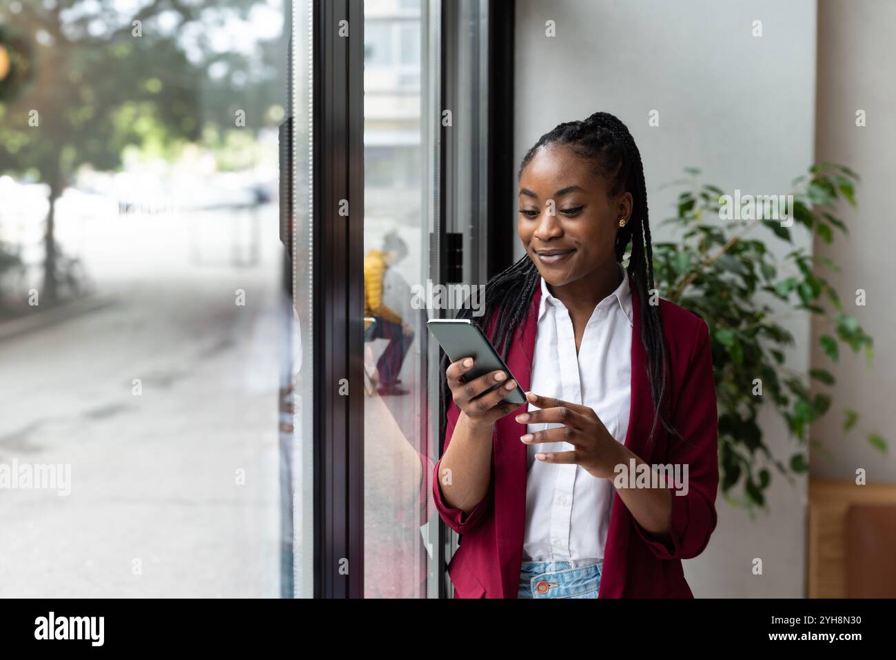 Femme d'affaires réfléchie utilisant un téléphone intelligent debout dans le bureau regardant par la fenêtre sur Big City. Charismatique Digital entrepreneur Plan investissement Banque D'Images