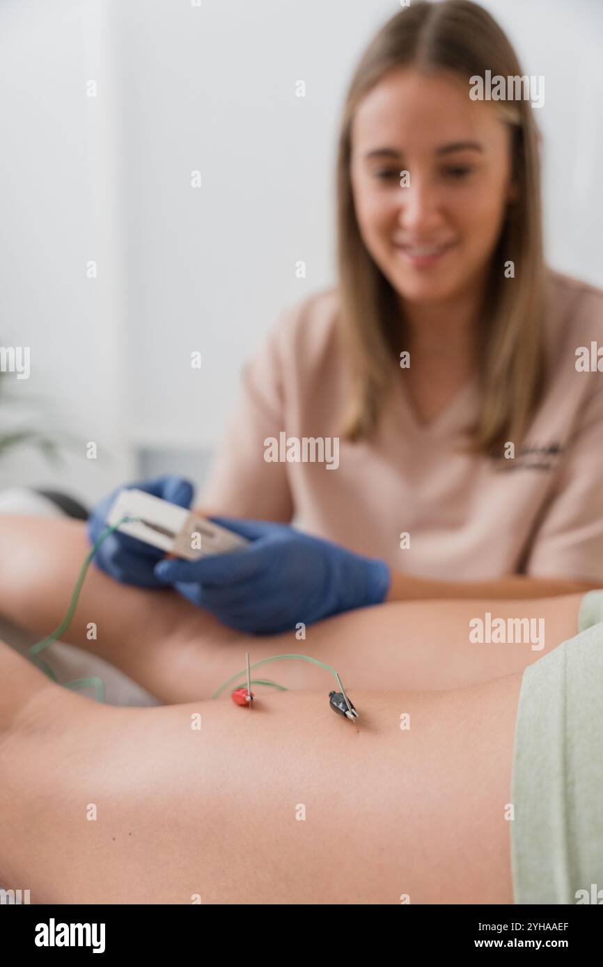 Physiothérapeute appliquant des aiguilles d'électroacupuncture à la jambe du patient pour soulager la douleur Banque D'Images