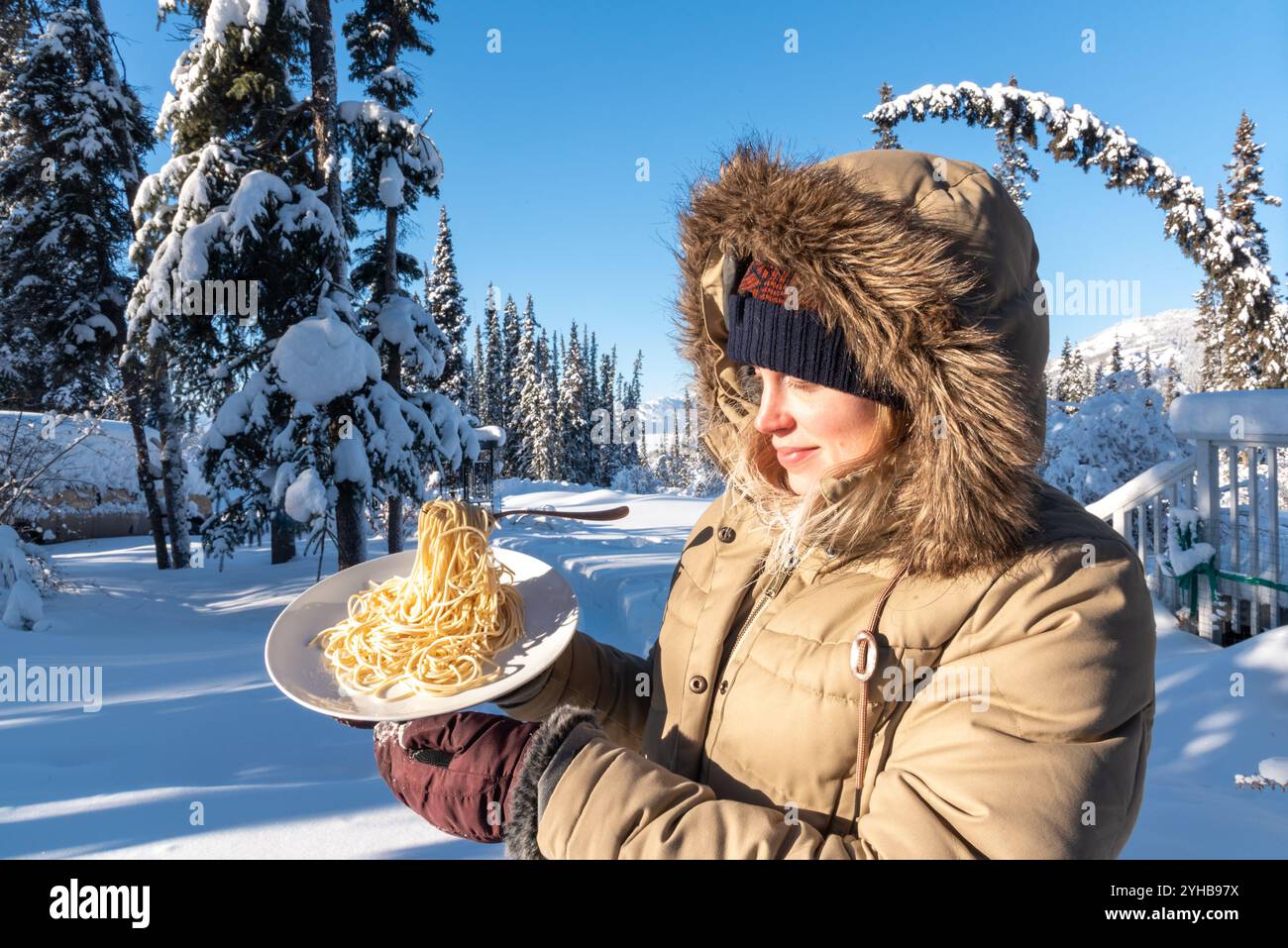 Femme debout à l'extérieur dans le paysage arctique froid du nord pendant le jour de température glaciale -40 tenant une assiette de nouilles de pâtes congelées avec fourchette. Banque D'Images