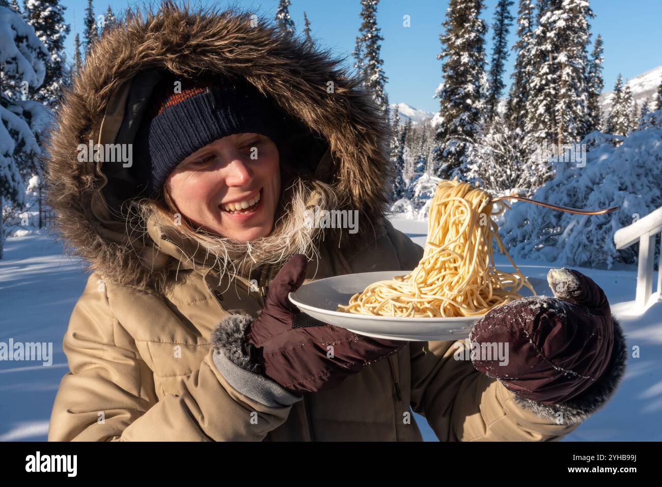 Femme debout à l'extérieur dans le paysage arctique froid du nord pendant le jour de température glaciale -40 tenant une assiette de nouilles de pâtes congelées avec fourchette. Banque D'Images