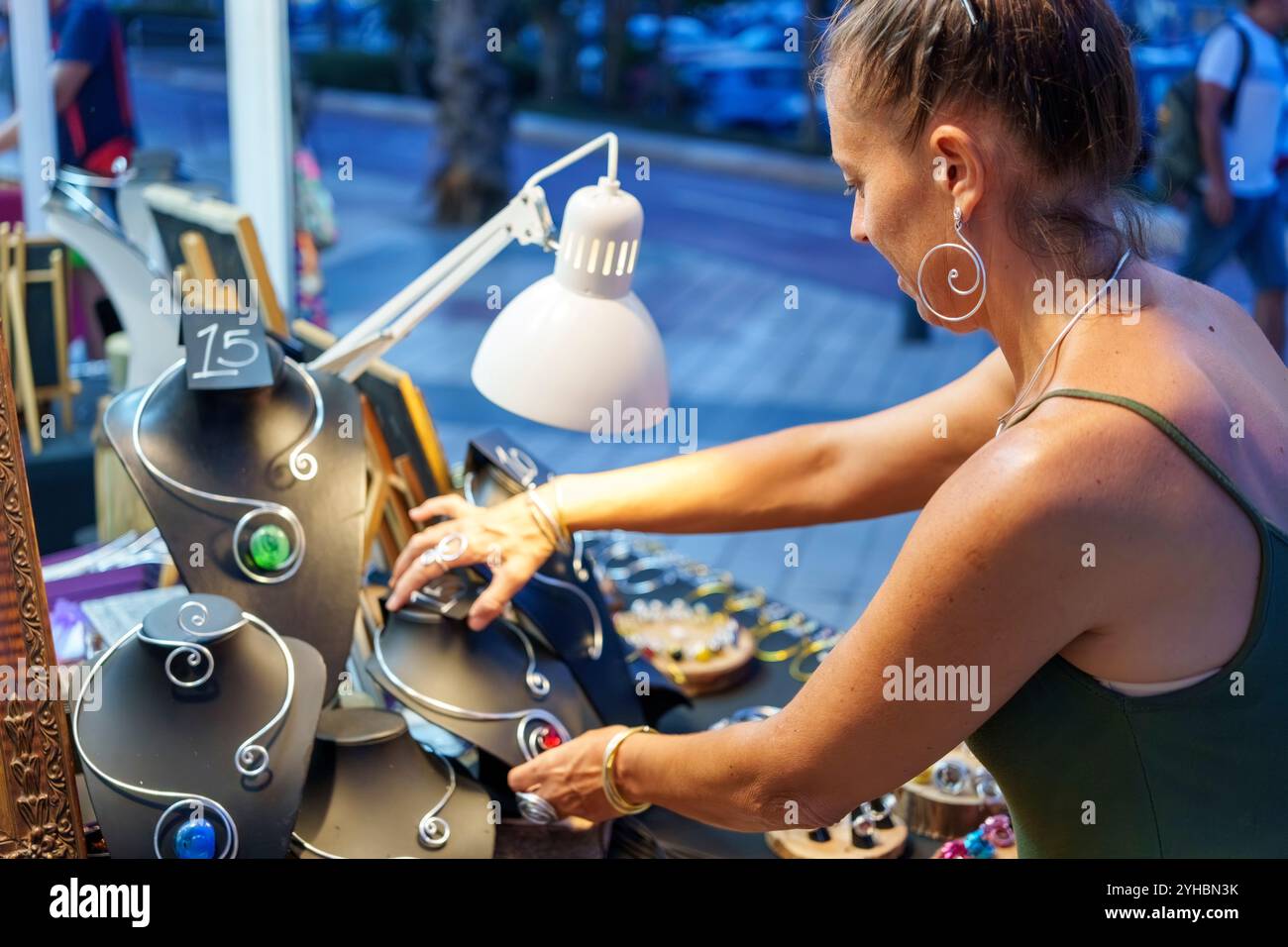 Femme mature organisant l'affichage de bijoux en fil d'aluminium faits à la main au stand de marché extérieur Banque D'Images