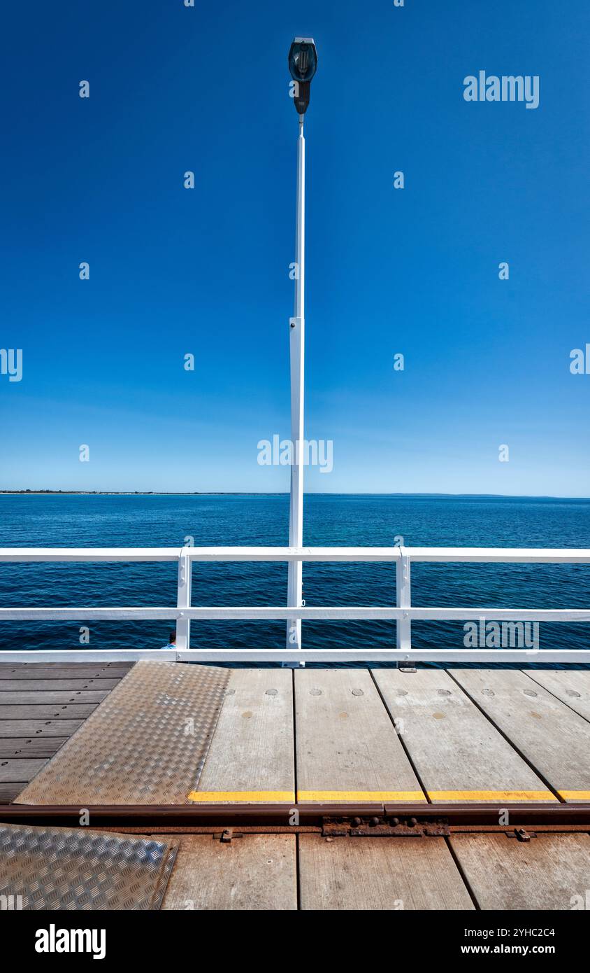 Une composition symétrique et géométrique d'une jetée avec un lampadaire blanc et une balustrade contre le ciel bleu et l'eau Banque D'Images