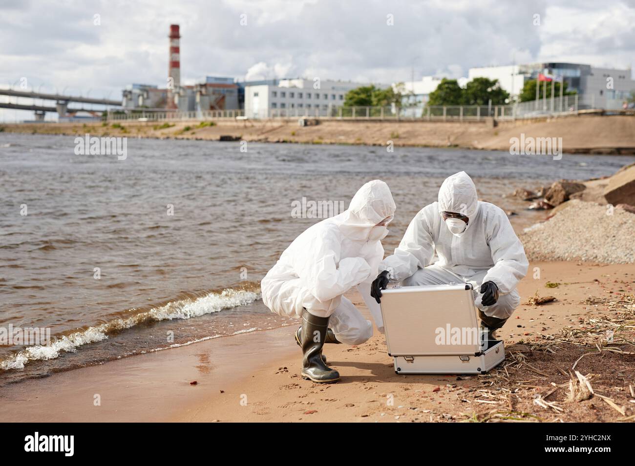 Vue grand angle à deux des scientifiques méconnaissables portant des combinaisons de matières dangereuses et ouvrant le kit de test tout en faisant des sondes sur l'eau à l'extérieur, copier l'espace Banque D'Images