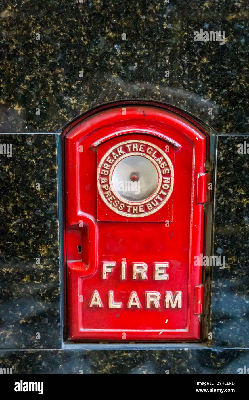 Ancien boîtier d'alarme incendie rouge monté sur un mur de granit avec des instructions pour une utilisation d'urgence dans un cadre de bâtiment public, Australie Banque D'Images