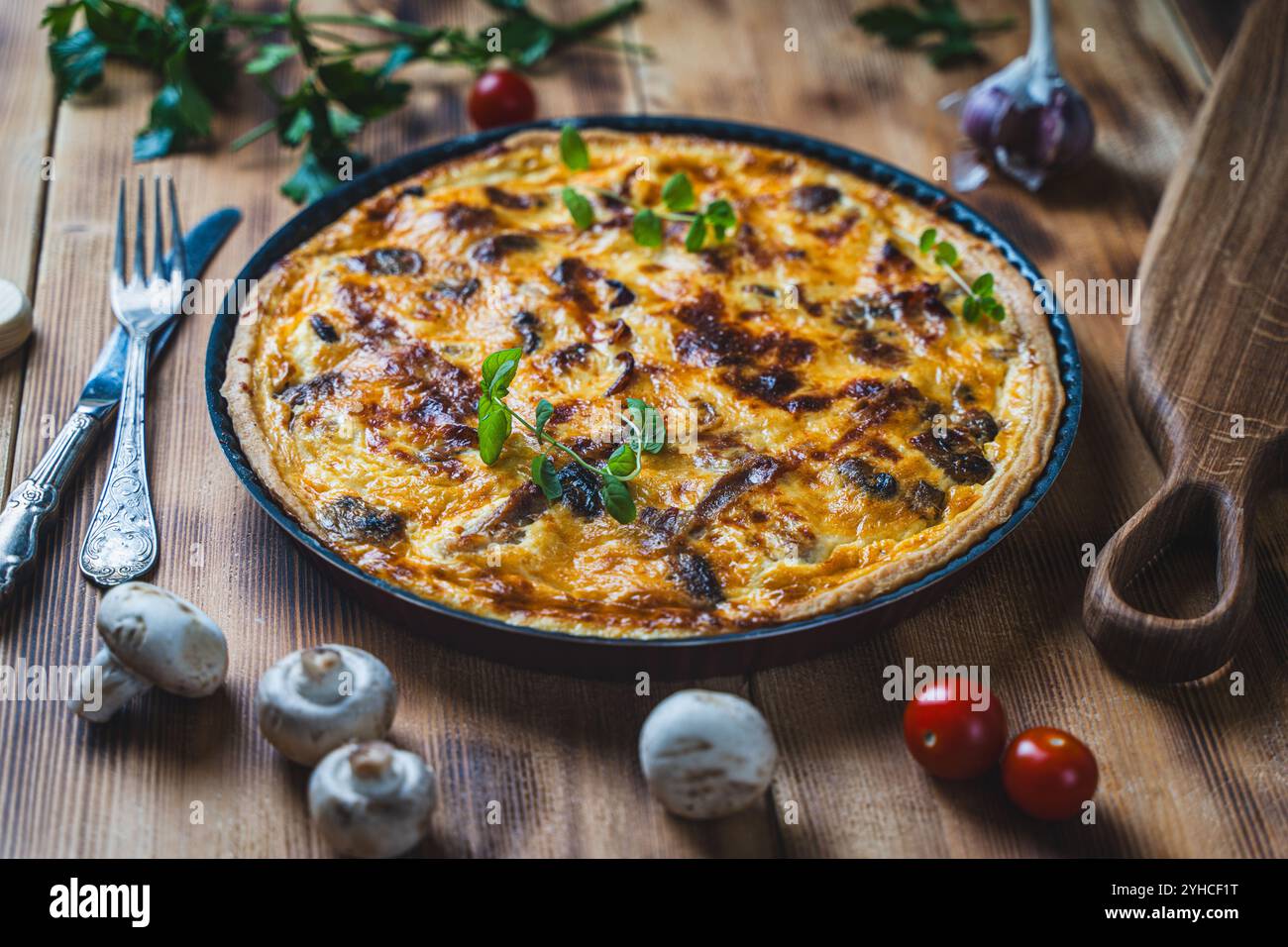 Quiche ou tarte avec de la viande, du poulet et des champignons sur une table en bois avec couverts, herbes et tomates cerises. Photo de haute qualité Banque D'Images