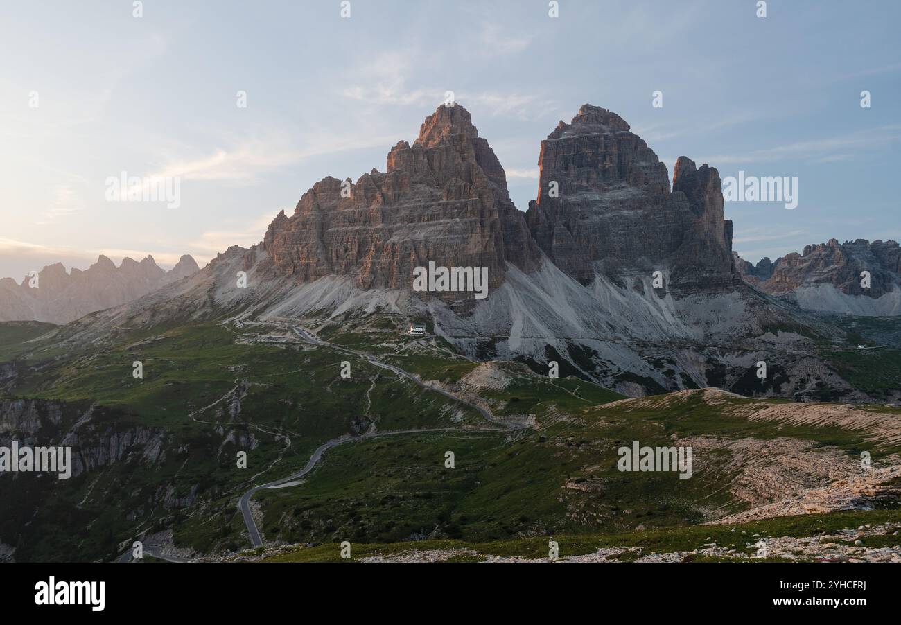 Coucher de soleil sur Tre Cime di Lavaredo dans les Dolomites, Italie. Les pics accidentés brillent par une lumière chaude, avec une route de montagne sinueuse en contrebas. Banque D'Images