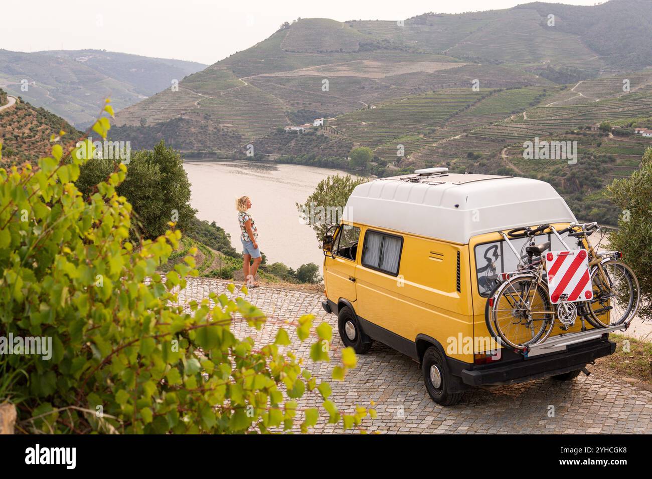 Femme blonde profitant de la vue debout près de son camping-car rétro garé dans la vallée du Douro, Portugal Banque D'Images