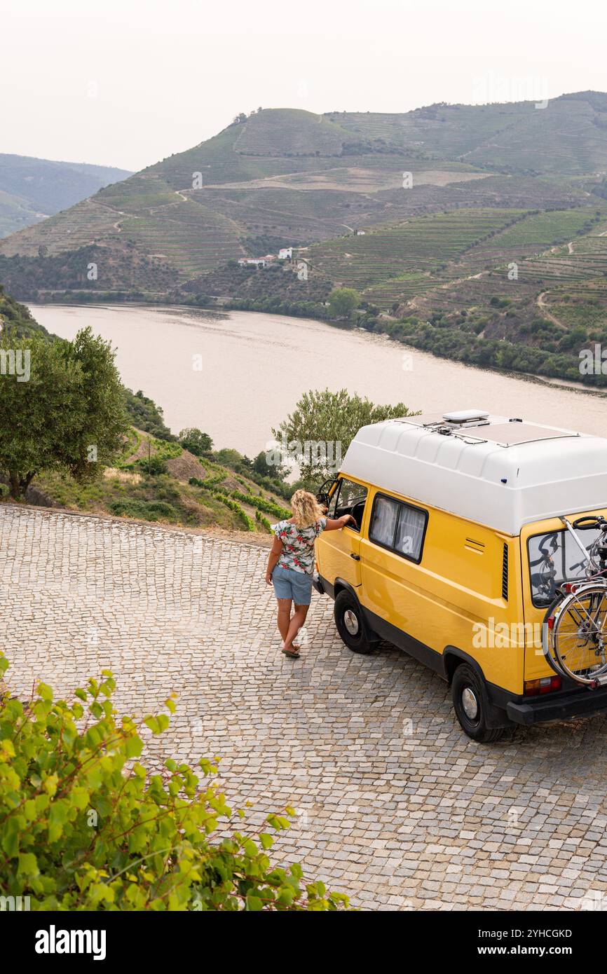 Femme blonde profitant de la vue debout près de son camping-car rétro garé dans la vallée du Douro, Portugal Banque D'Images