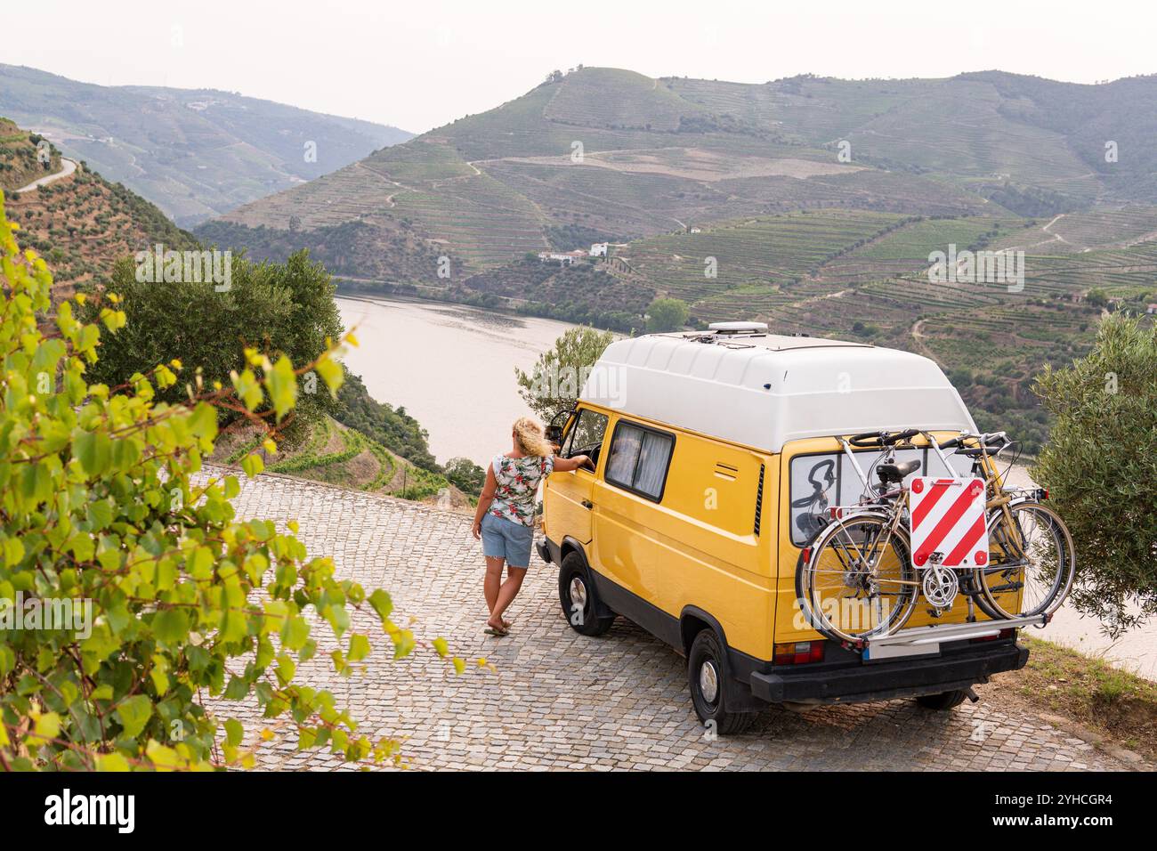 Femme blonde profitant de la vue debout près de son camping-car rétro garé dans la vallée du Douro, Portugal Banque D'Images