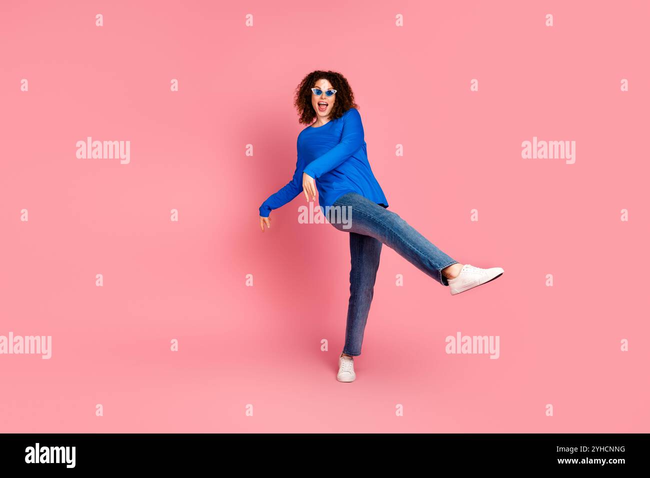 Jeune femme avec les cheveux roux dans une tenue décontractée profitant d'un moment ludique sur fond rose Banque D'Images