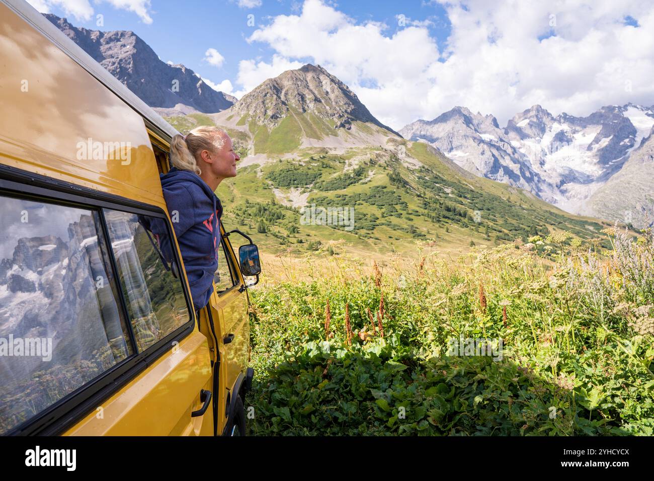 Jeune femme blonde profitant de la vue sur les montagnes dans son camping-car jaune rétro dans le parc national des Ecrins, France Banque D'Images