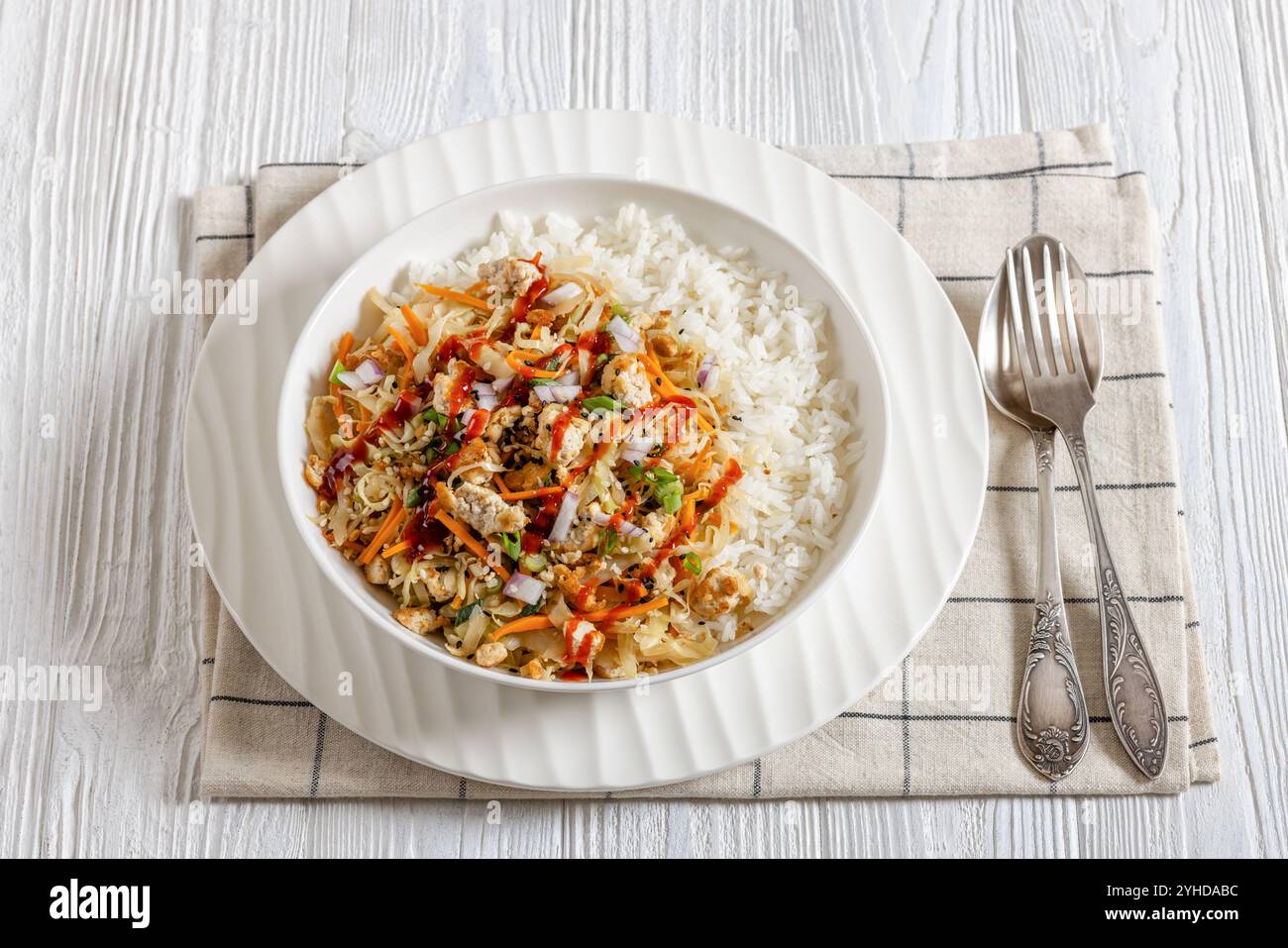roulé aux œufs de tofu, chou sautés, tofu émietté assaisonné servi dans une sauce sucrée et salée servie sur du riz dans un bol sur une table en bois blanc avec fourchette Banque D'Images