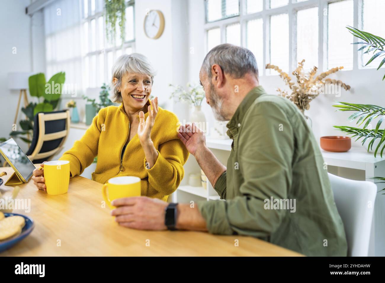 Charmant couple mature profitant du café du matin à la maison assis sur la table du salon et bavarder joyeusement Banque D'Images