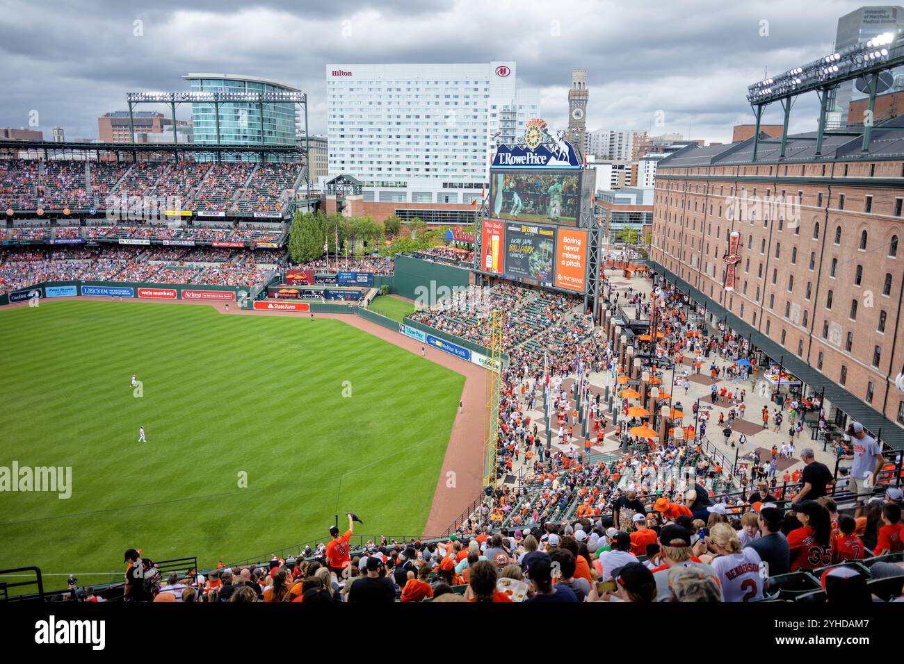 Match de baseball au Oriole Park At Camden Yards à Baltimore | BALTIMORE, Maryland — Un match de baseball se déroule au Oriole Park At Camden Yards, le terrain maison des Baltimore Orioles. Le stade, inauguré en 1992, a établi le standard pour la conception rétro-classique des stades de la Major League Baseball. L’entrepôt emblématique B&O sert de toile de fond pour le champ droit du stade. Banque D'Images