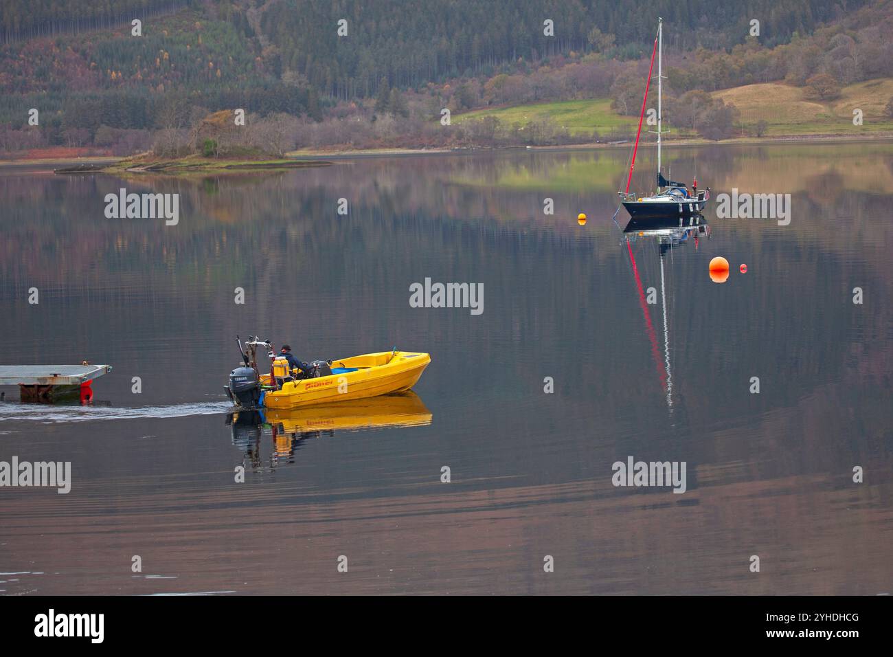 Lochaber, Écosse, Royaume-Uni. 11 novembre 2024. Temps nuageux dans les Highlands écossais avec une température autour de 11 degrés centigrades. Sur la photo : petit bateau à moteur jaune quittant la jetée avec un voilier reflété dans les eaux calmes du Loch Leven, Ballachulish, Lochaber. Credit : Archwhite/Alamy Live news. Banque D'Images