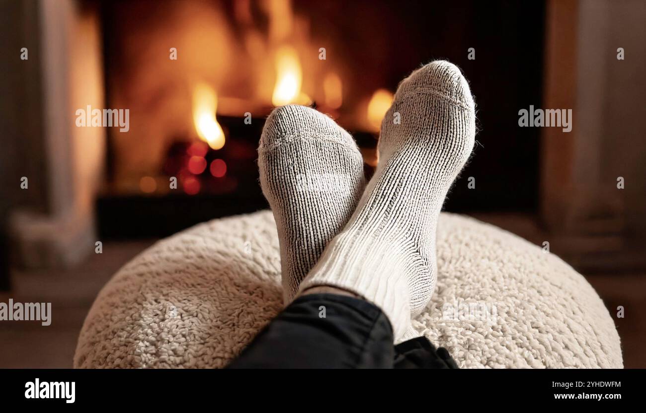 Pieds adultes confortables devant le feu dans des chaussettes tricotées en laine chaude beige clair couleur flocons d'avoine, reposant sur un tabouret en tissu boucle blanc neutre dans le lounge Li Banque D'Images