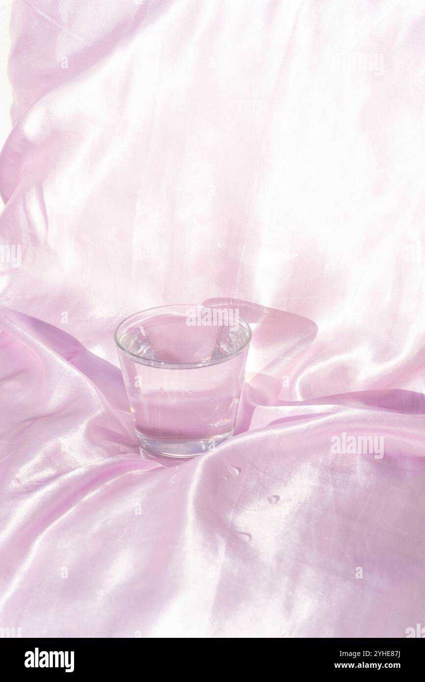 Verre élégant d'eau sur fond de tissu rose doux Banque D'Images