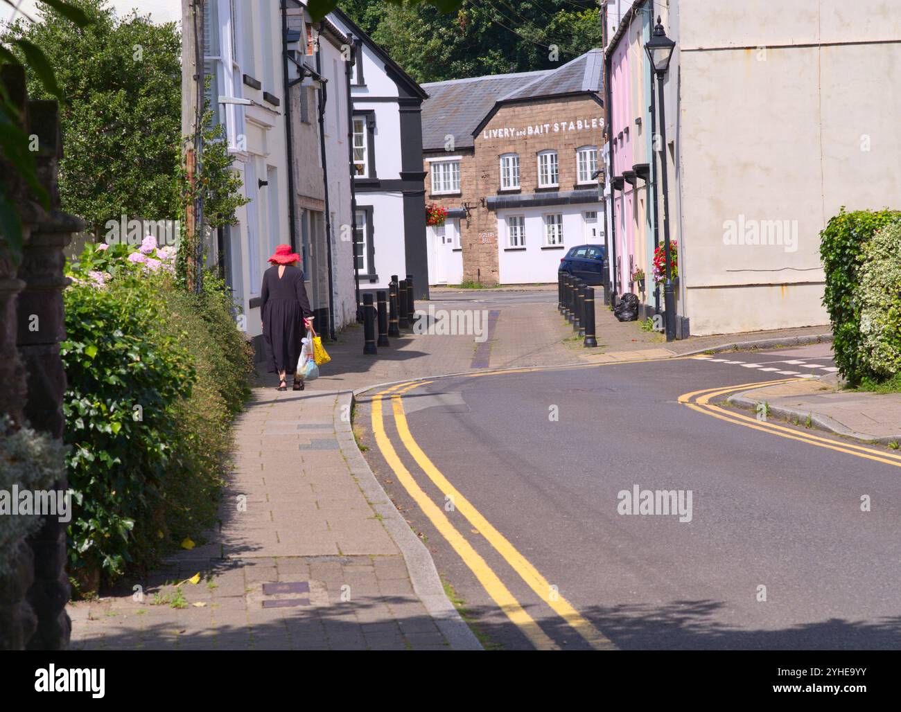 Femme en robe noire et chapeau rouge marchant tristement seule avec ses courses. USK market Town, pays de Galles du Sud. ROYAUME-UNI Banque D'Images