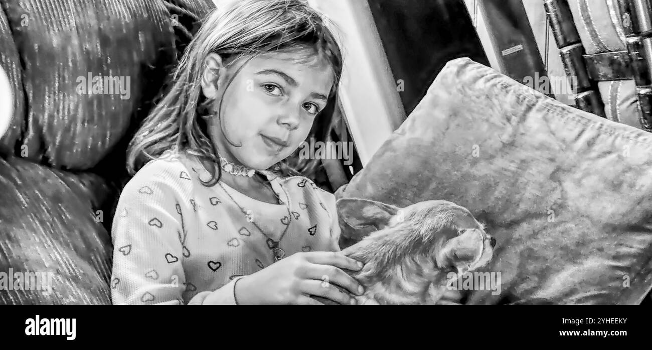 Photo en noir et blanc d'une jeune fille tenant un chihuahua assis sur une chaise Banque D'Images
