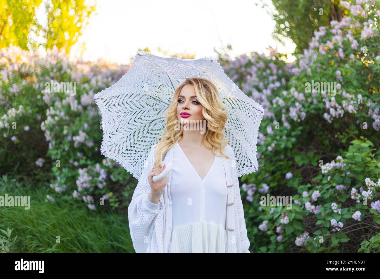 Jeune belle femme en robe historique blanche et coiffe debout avec parapluie parmi les arbres avec des fleurs de lilas. Portrait historique d'aristocratique Banque D'Images