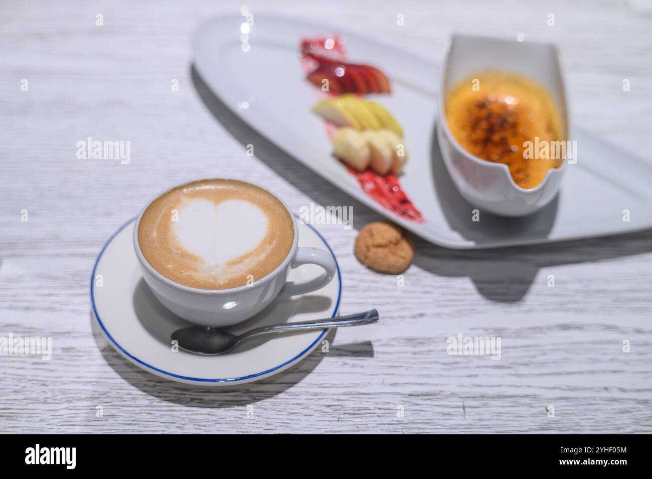 Un latte magnifiquement conçu avec un motif coeur accompagné d'une sélection de fruits et d'un dessert riche crème anglaise. Banque D'Images