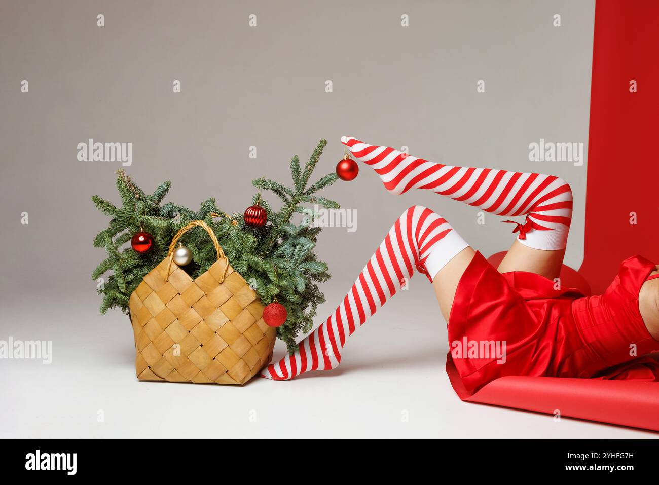 jambes de fille en bas rouges et blancs rayés décorent l'arbre de noël dans un panier décoré de boules rouges, concept de noël créatif Banque D'Images