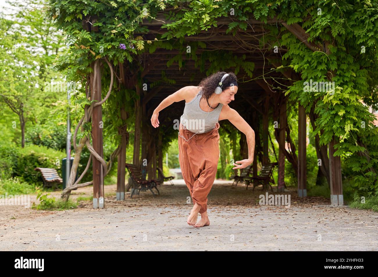 Une danseuse contemporaine se déplace gracieusement dans un parc, immergée dans la musique à travers des écouteurs, mêlant art et sérénité de la nature. Banque D'Images