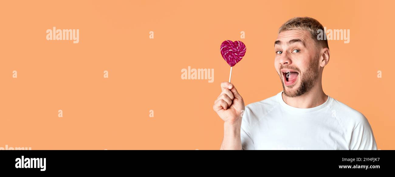 Homme émotionnel avec la bouche ouverte tient coeur lollipop Banque D'Images