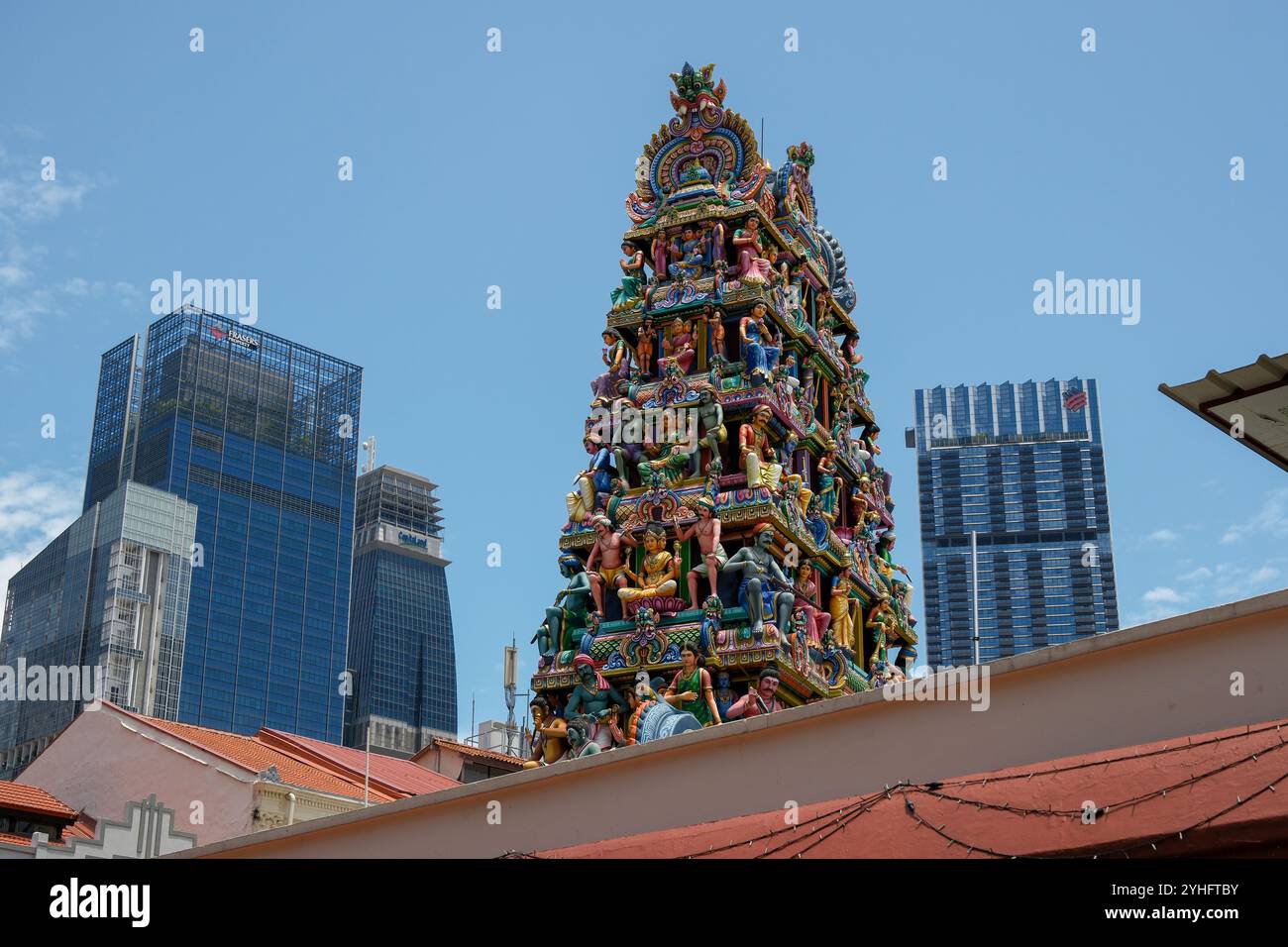 La tour Gopuram du temple Sri Mariamman présente des sculptures en plâtre aux couleurs vives contrastant avec un ciel bleu et des gratte-ciels modernes. Banque D'Images