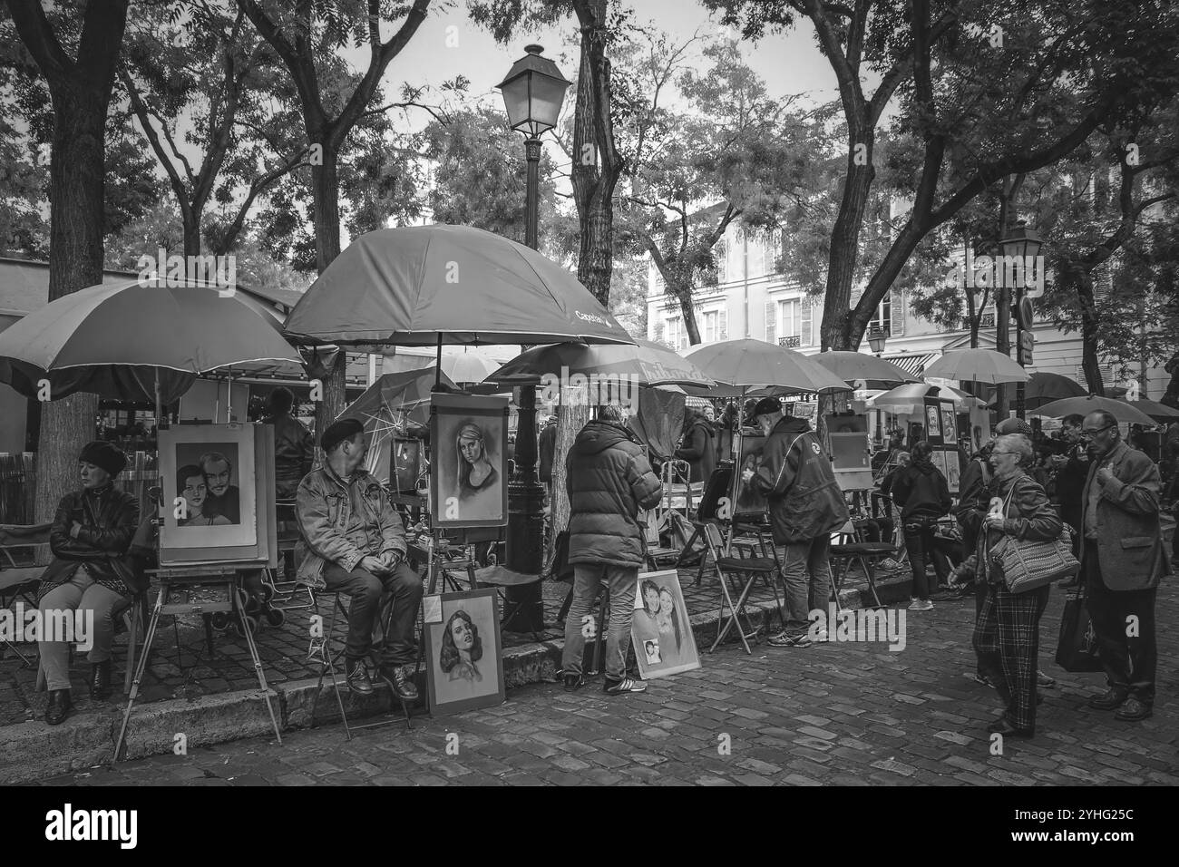 Artistes avec leurs portraits à vendre sous parapluies, capturant une scène de rue parisienne, photographiée en noir et blanc. Banque D'Images