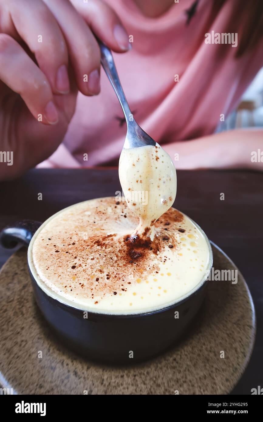 Gros plan d'une personne dégustant du café traditionnel vietnamien au jaune d'œuf, connu sous le nom de « Cà Phê Trứng ». La mousse épaisse et crémeuse montre sa richesse unique. Banque D'Images