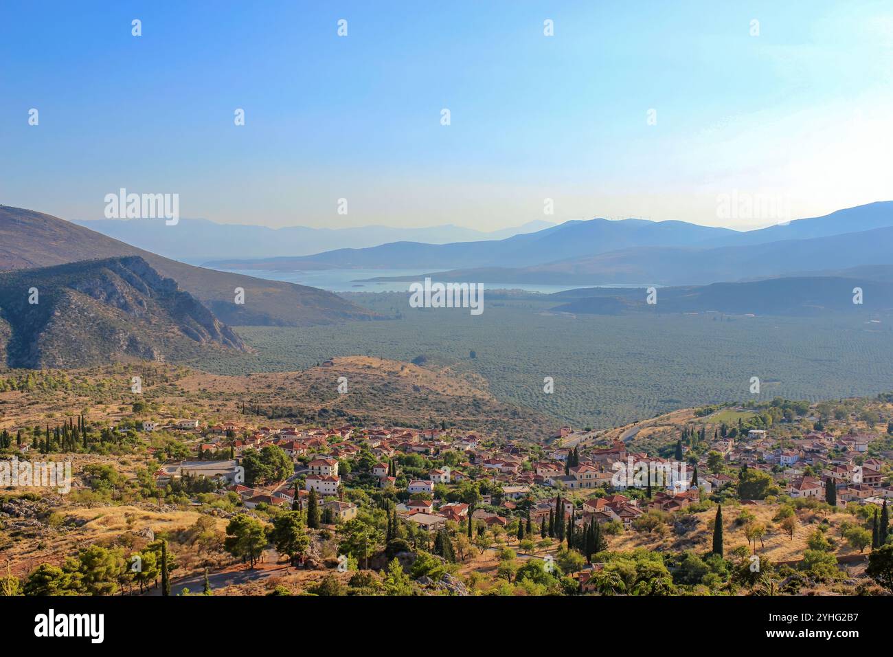 Une vue panoramique avec des oliveraies tentaculaires, des montagnes lointaines et des eaux sereines sous un ciel clair, mettant en valeur la beauté naturelle de la région. Banque D'Images