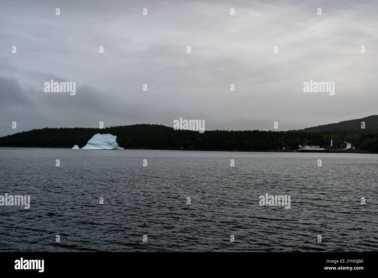 Un iceberg est pris au piège dans une baie tranquille près d'un terminal de ferry, entouré d'arbres et d'eau, mélangeant merveille naturelle avec le bourdonnement subtil des ferries Banque D'Images