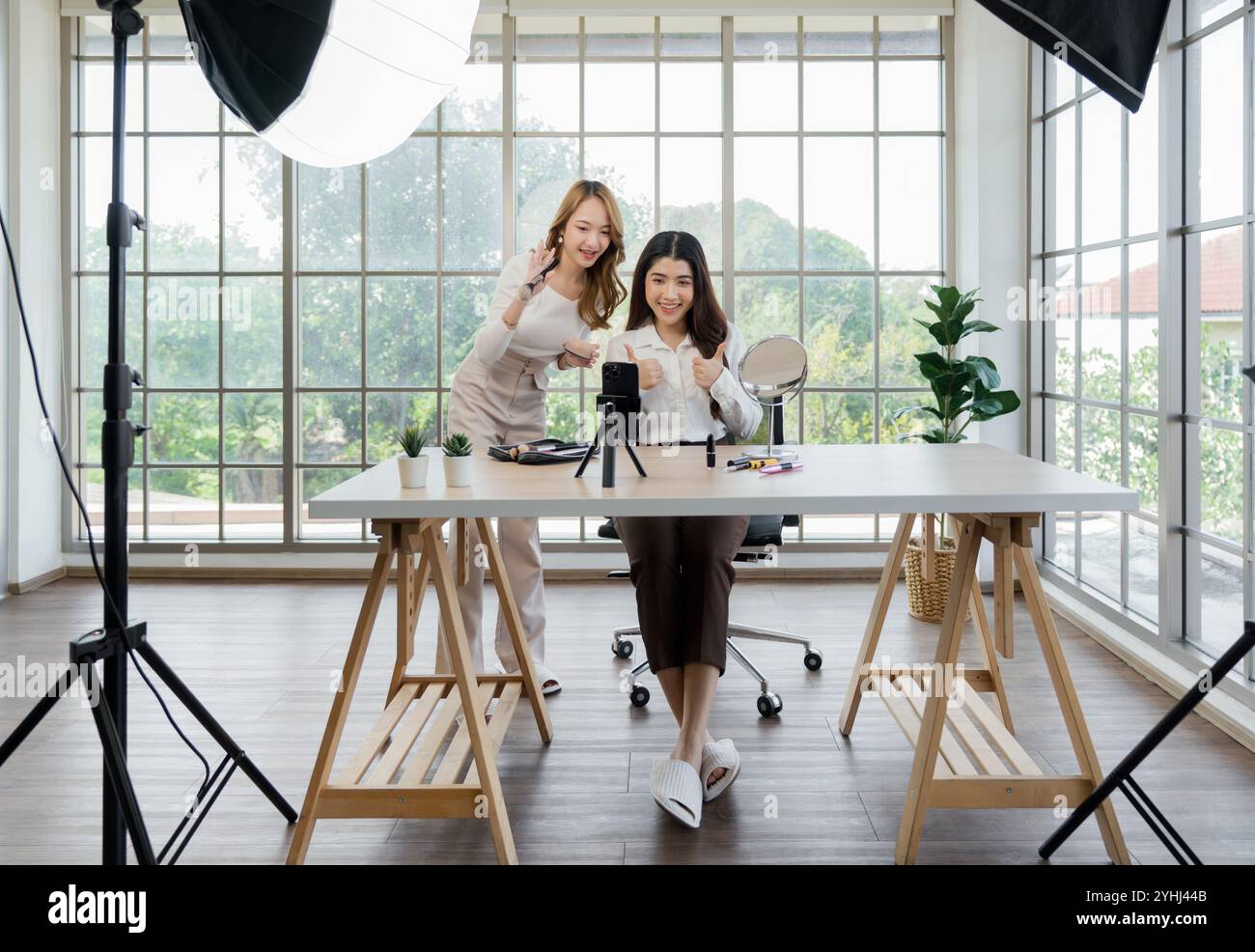 Deux femmes asiatiques créant du contenu pour les médias sociaux. Ils utilisent une configuration de studio qui comprend un smartphone monté sur un trépied, un équipement d'éclairage et Banque D'Images