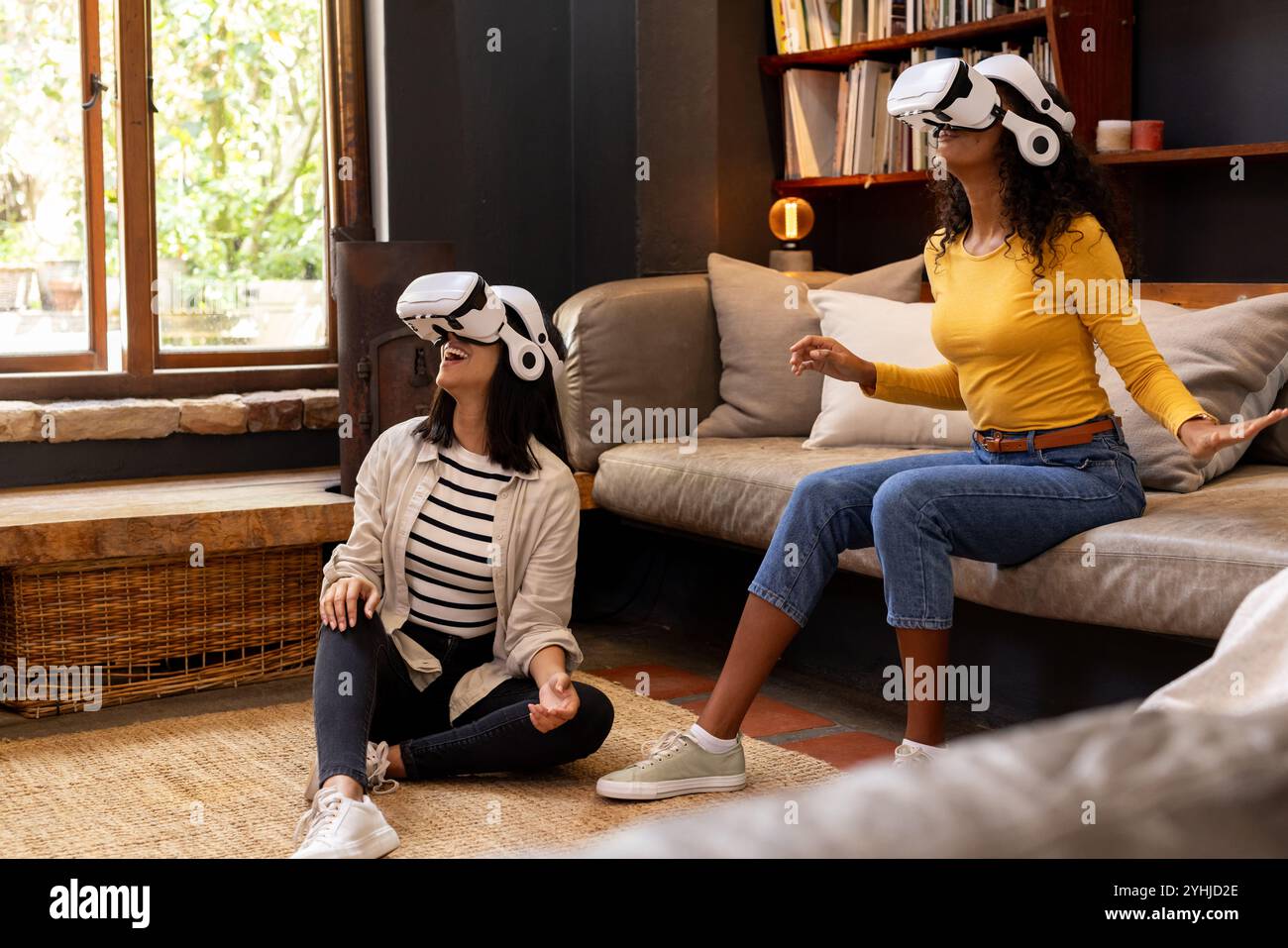 Amies féminines multiraciales profitant de l'expérience de réalité virtuelle à la maison, assis sur le sol Banque D'Images
