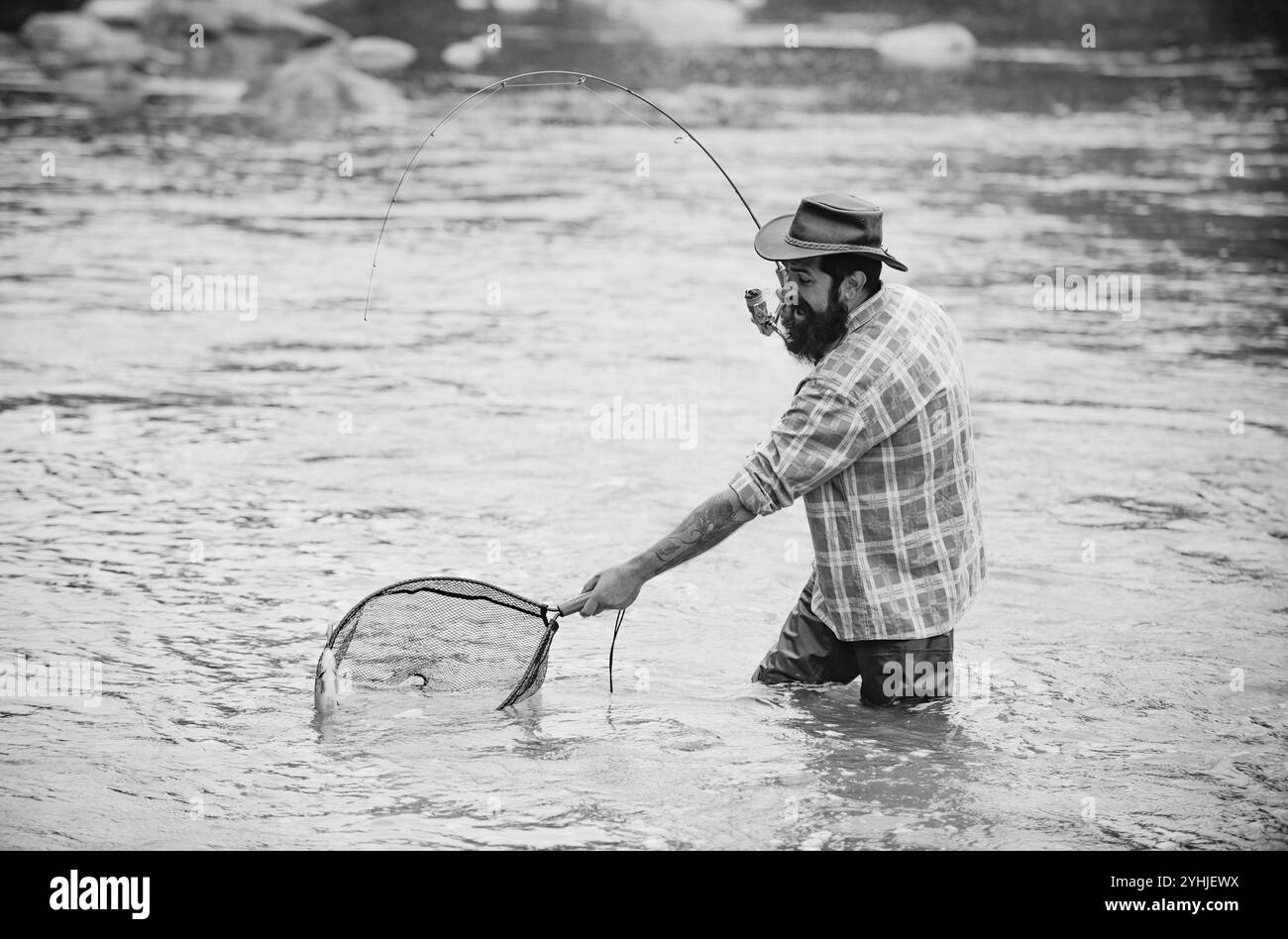 Jeune homme pêchant. Pêcheur avec canne, moulinet sur la rive de la rivière. Homme attrapant des poissons, tirant la canne tout en pêchant sur le lac. Nature sauvage. Attraper la truite Banque D'Images