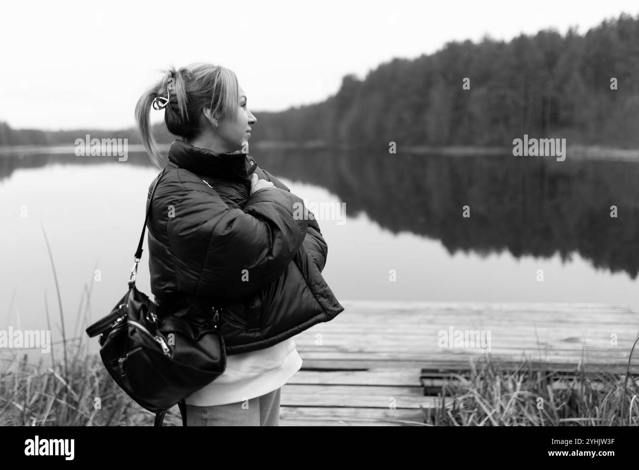 Une jeune femme se tient près du lac calme, réfléchissant dans l'eau calme, entourée d'arbres par une journée nuageuse Banque D'Images