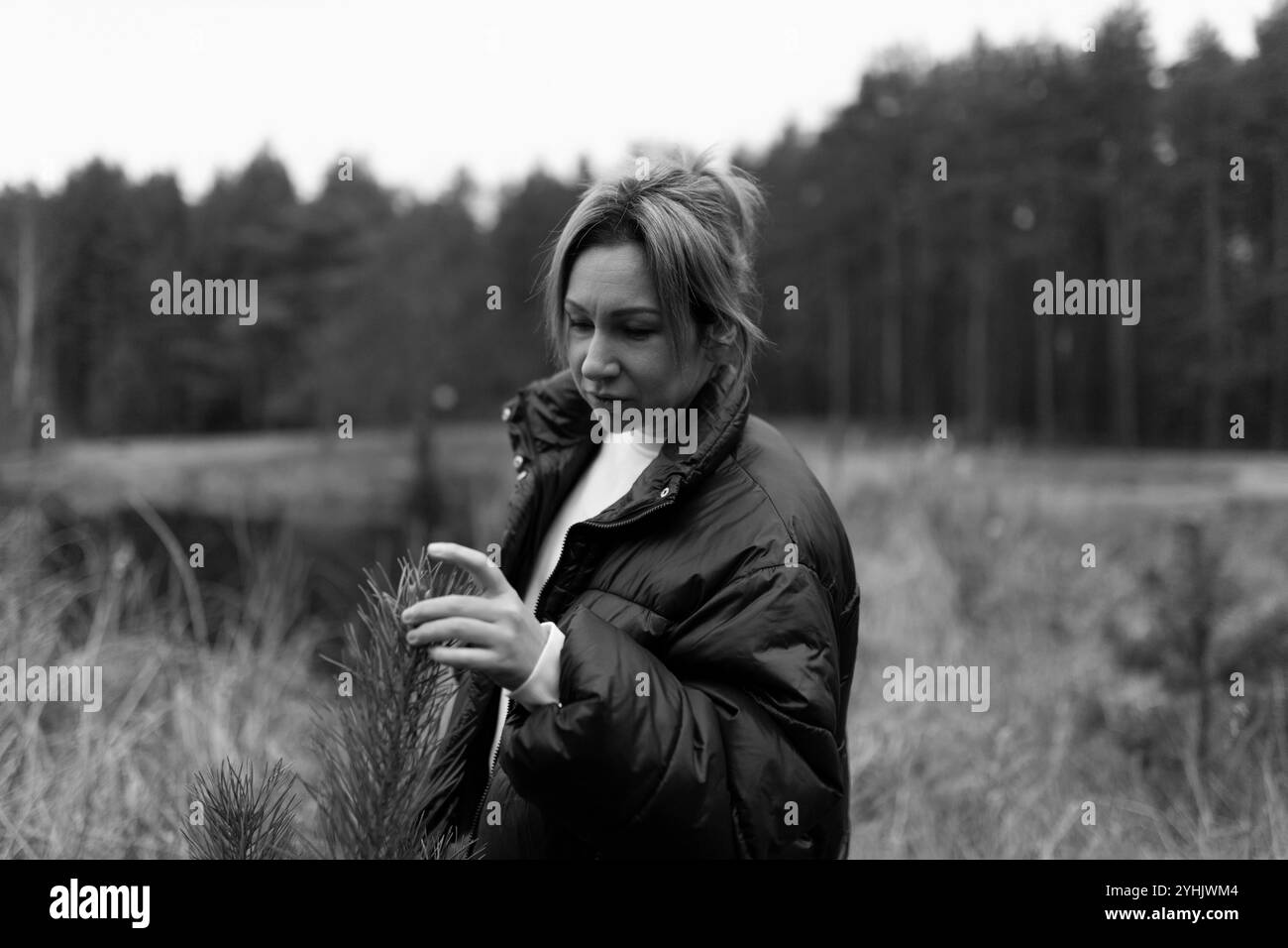 Femme explorant la nature dans une zone boisée, appréciant les détails de la verdure pendant une journée nuageuse en automne Banque D'Images