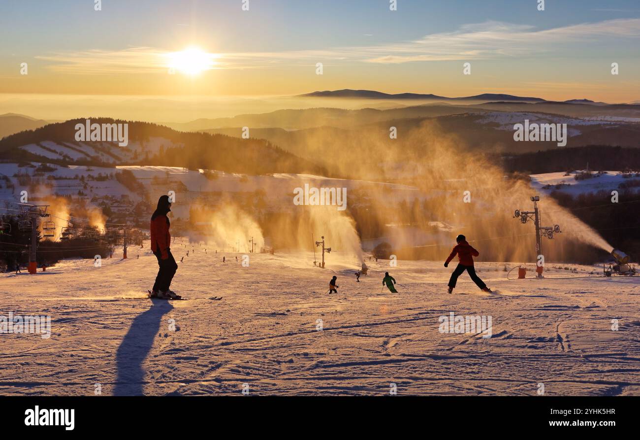 Piste de ski dans la station d'hiver avec des skieurs et des canons à neige au coucher du soleil, Slovaquie Banque D'Images