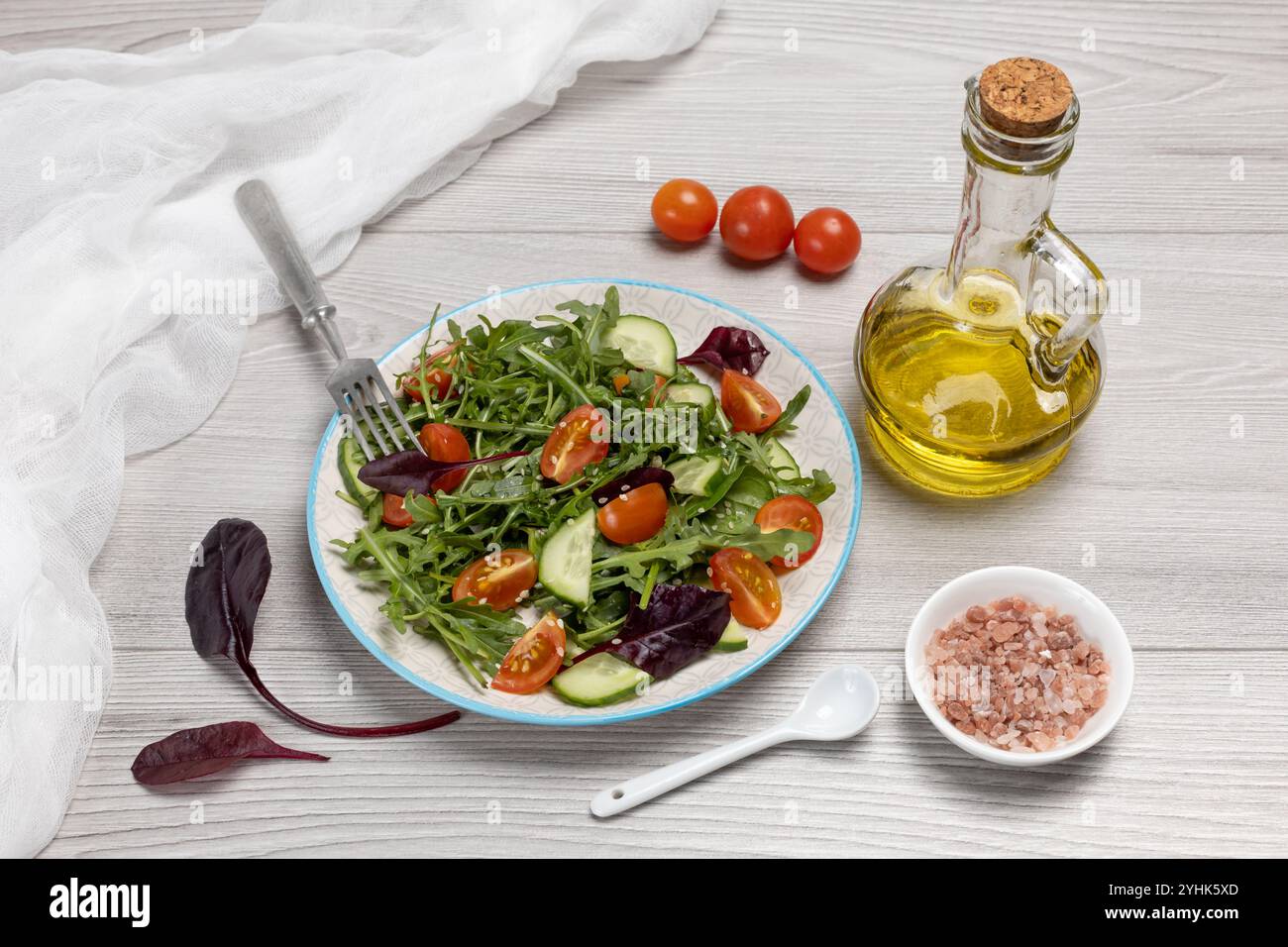 Salade avec tomates fraîches, concombres, roquette, basilic, épinards sur l'assiette avec une fourchette. Bouteille d'huile d'olive. Bol avec du sel. Régime végétal sain Banque D'Images