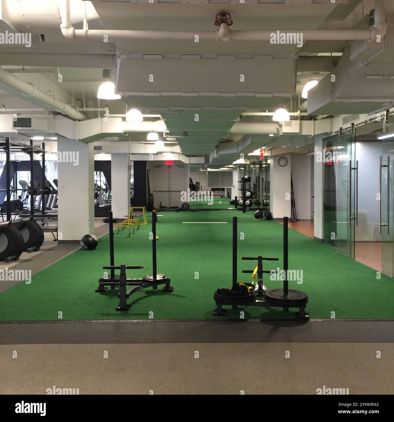 Intérieur de salle de sport moderne avec gazon vert pour pousser en traîneau, équipement de musculation et stations d'entraînement. Éclairage spacieux et lumineux, avec des murs en verre clair. Banque D'Images