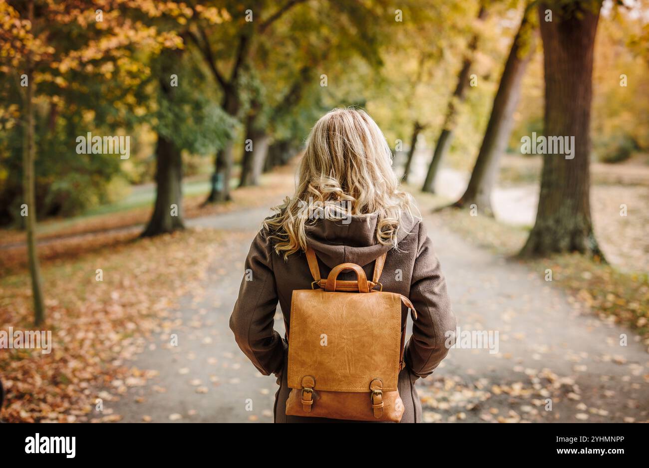 Femme élégante avec manteau brun et sac à dos promenades dans le parc d'automne. Beauté et mode de vie Banque D'Images